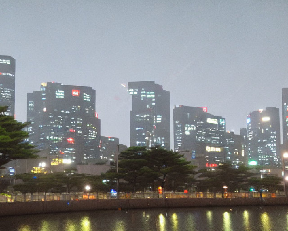 Night cityscape with glowing skyscrapers and fog, reflected in water, tree silhouette.