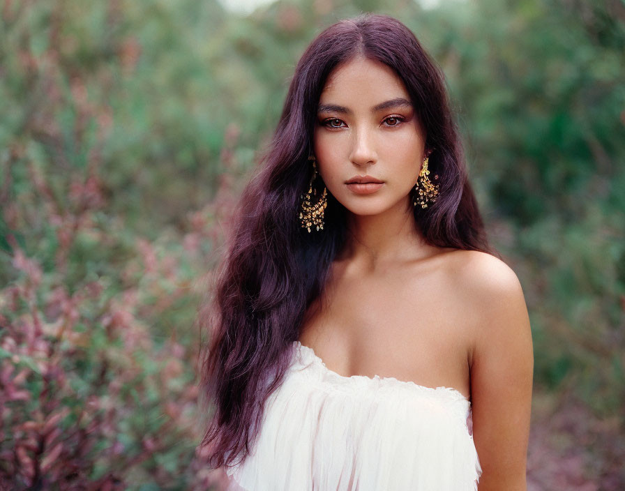 Woman with Dark Hair in Off-Shoulder White Dress and Gold Earrings Against Greenery