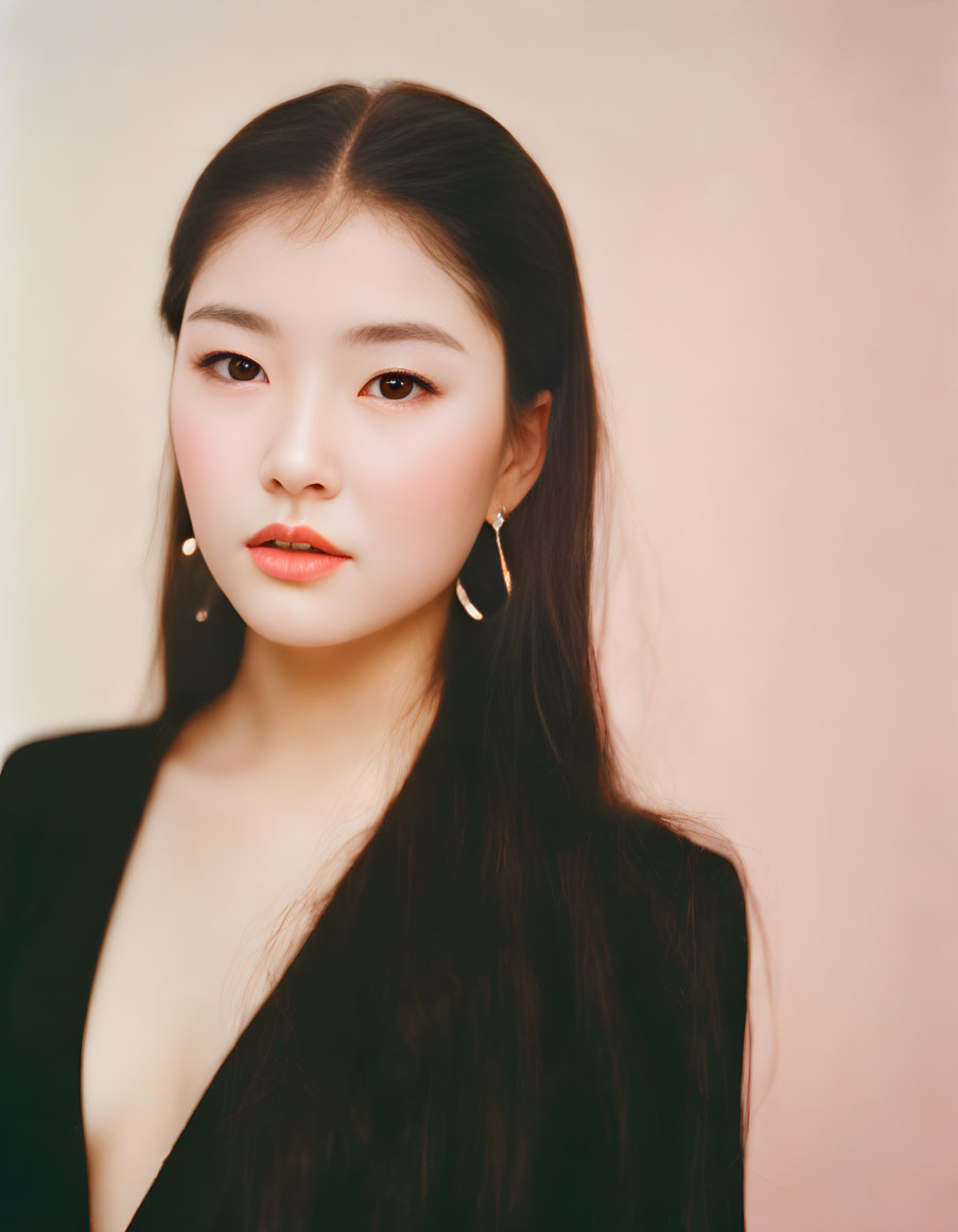 Portrait of young woman with dark hair in gold hoop earrings against soft pink background