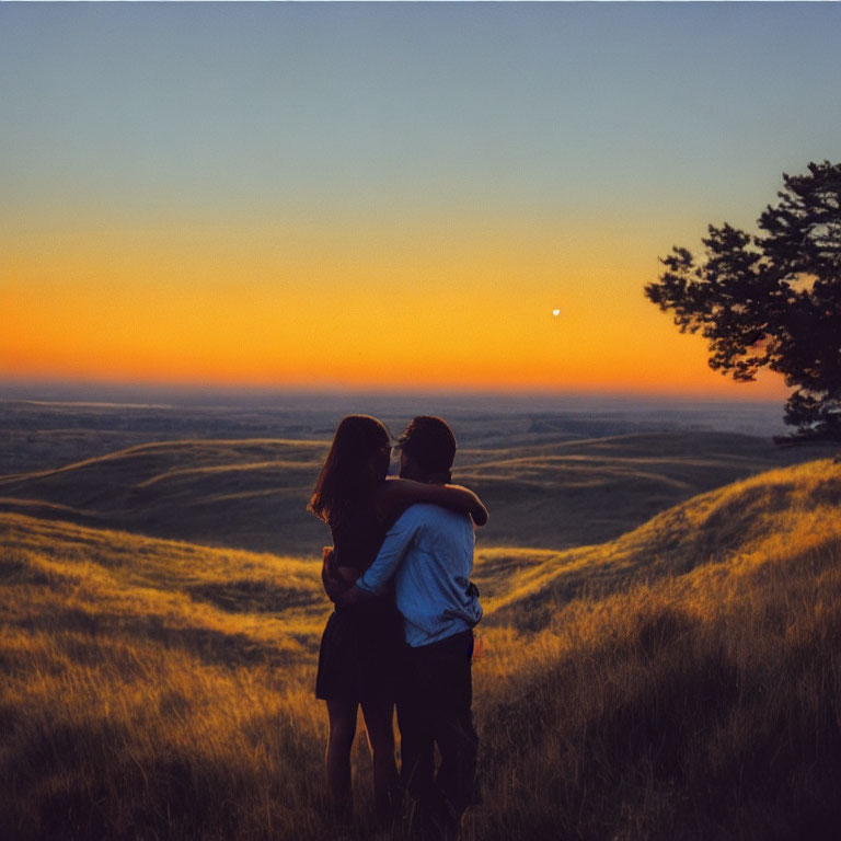 Embracing couple with sunset over hilly landscape