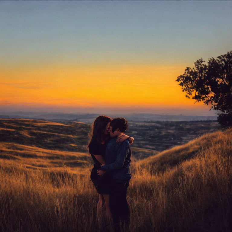 Romantic couple kissing on hill at sunset with golden grass and vibrant sky