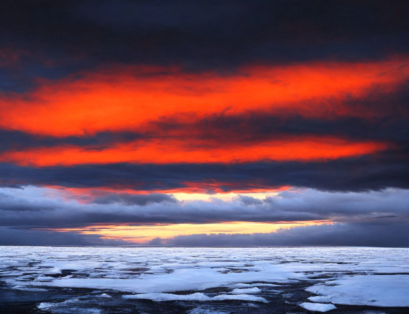 Vibrant sunset illuminating frozen landscape with ice and snow under dramatic sky