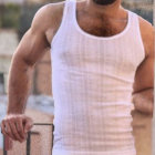 Silver-Haired Man in White T-Shirt Sitting on Railing with Cityscape Background