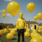 Yellow Masked Person Surrounded by Yellow Balloons in Field