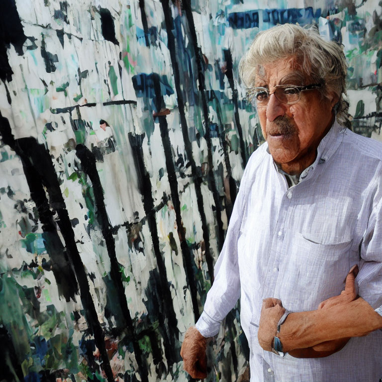 Elderly man with glasses in front of abstract painting.