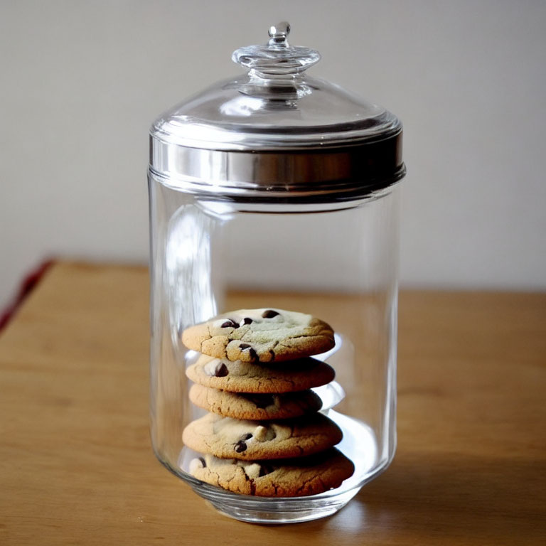 Transparent Glass Cookie Jar with Silver Lid and Chocolate Chip Cookies on Wooden Table