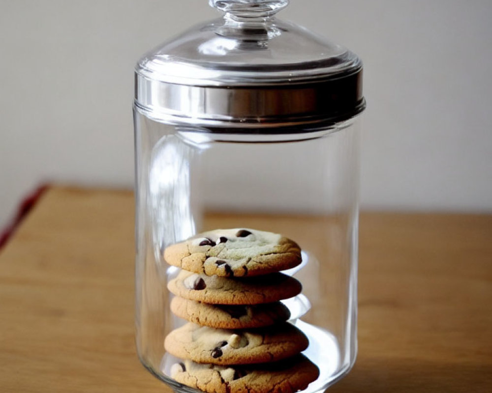 Transparent Glass Cookie Jar with Silver Lid and Chocolate Chip Cookies on Wooden Table