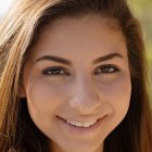 Smiling young woman with long brown hair and dark eyes in soft sunlight