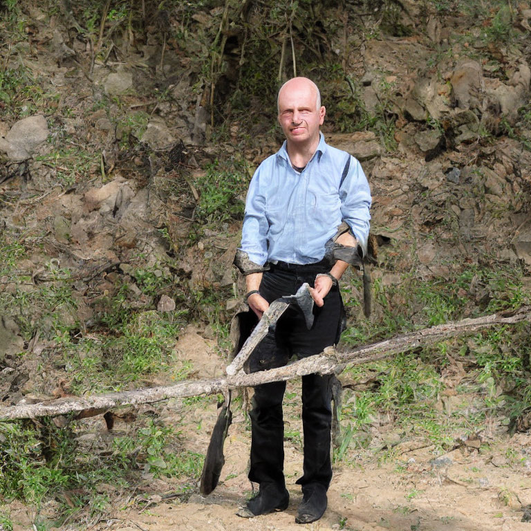 Bald man in blue shirt holding stick outdoors