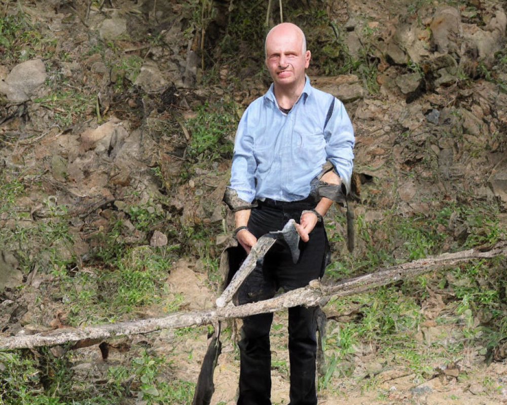 Bald man in blue shirt holding stick outdoors