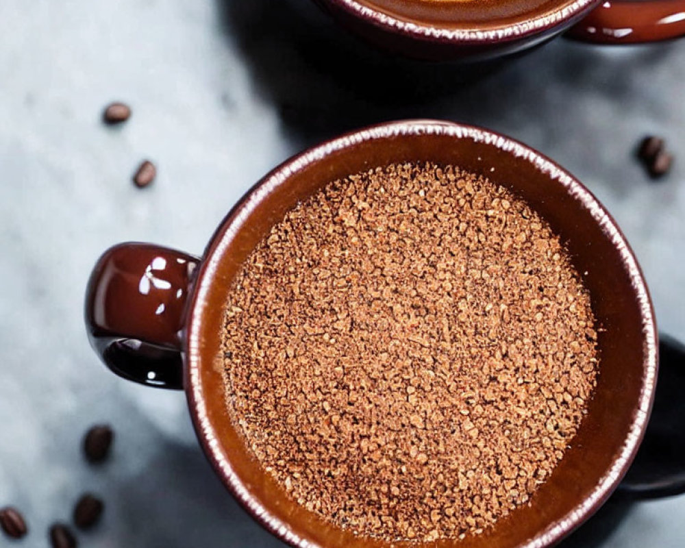 Two mugs with frothy coffee and coffee grounds on textured surface