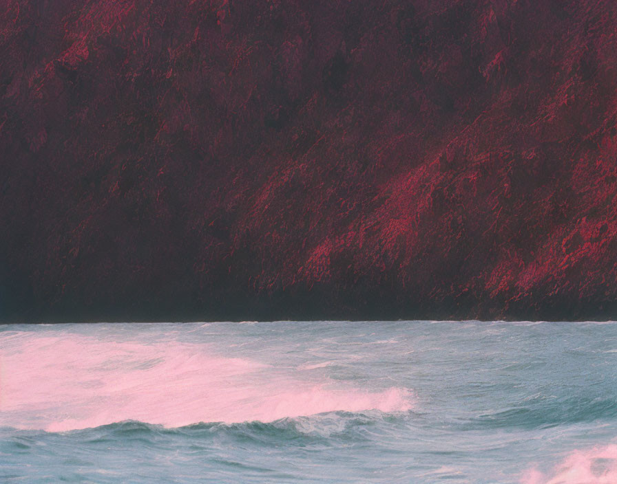 Twilight ocean waves near cliff under pink sky