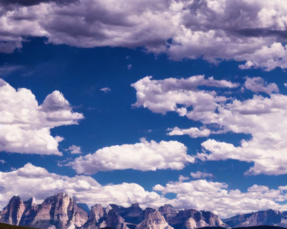 Majestic mountains under dramatic sky with fluffy clouds and dense forest.