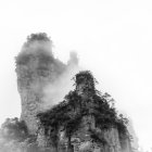 Solitary figure on misty peak gazes at fog-covered cliffs