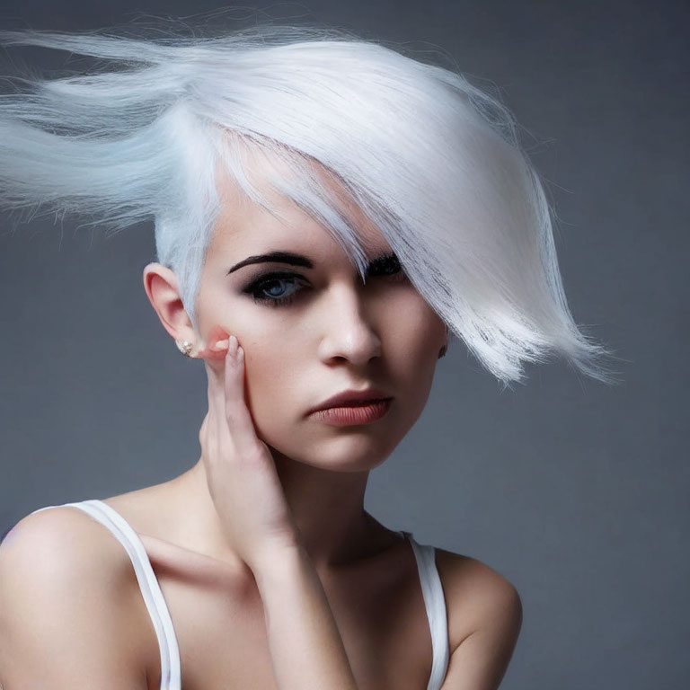 Striking white-haired woman with hand on cheek against grey background