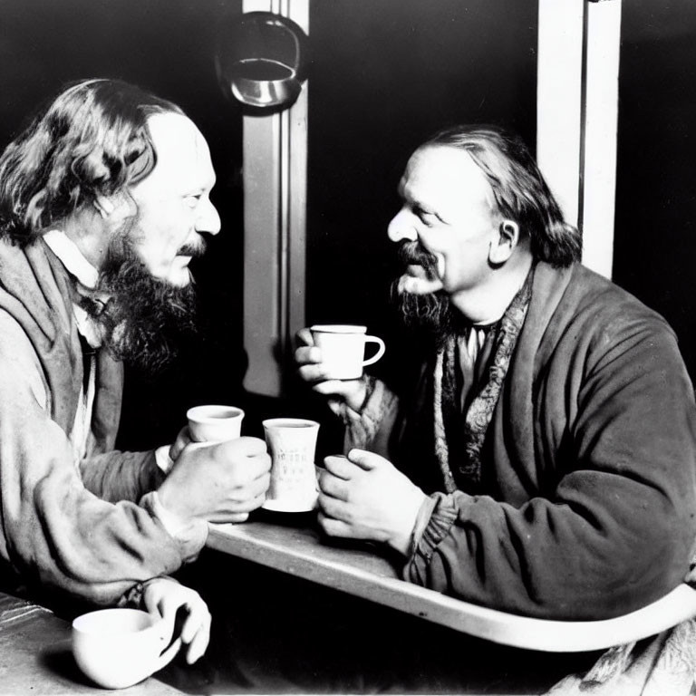 Two identical people chatting at a table with cups in hand.