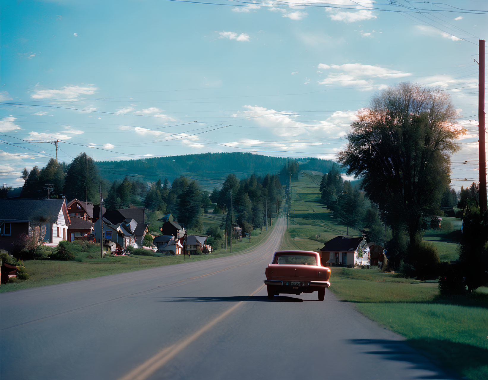 Vintage Red Car Driving on Tranquil Rural Road at Dusk