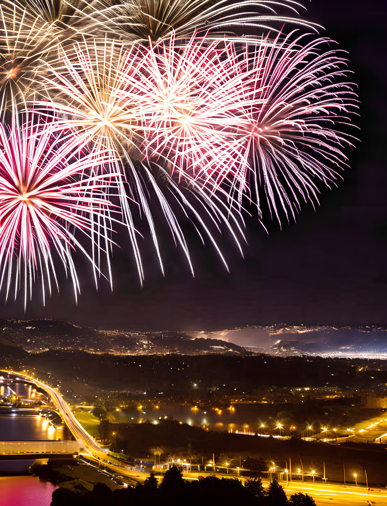 Colorful pink and white fireworks illuminate city skyline at night