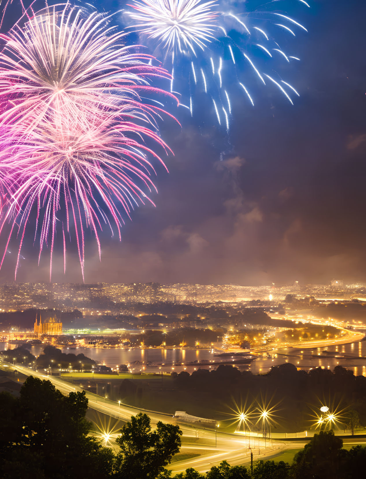 Colorful fireworks illuminate night sky over cityscape and river.