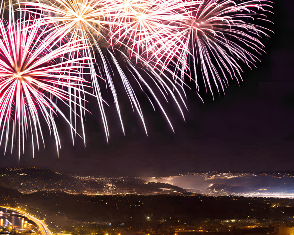 Colorful pink and white fireworks illuminate city skyline at night