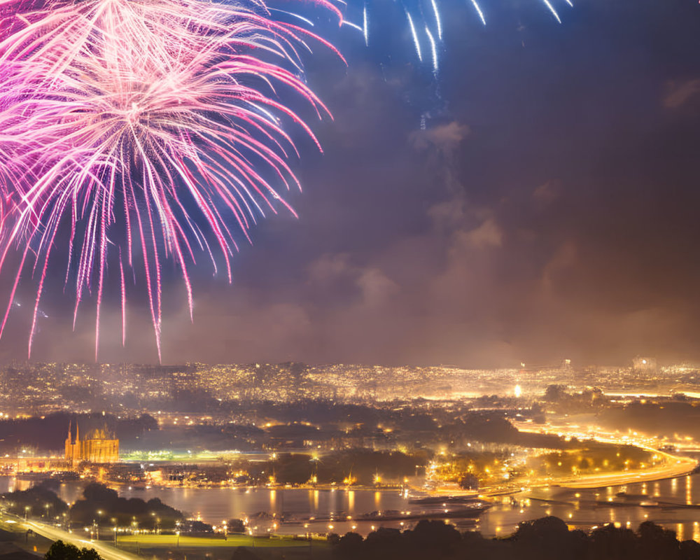 Colorful fireworks illuminate night sky over cityscape and river.