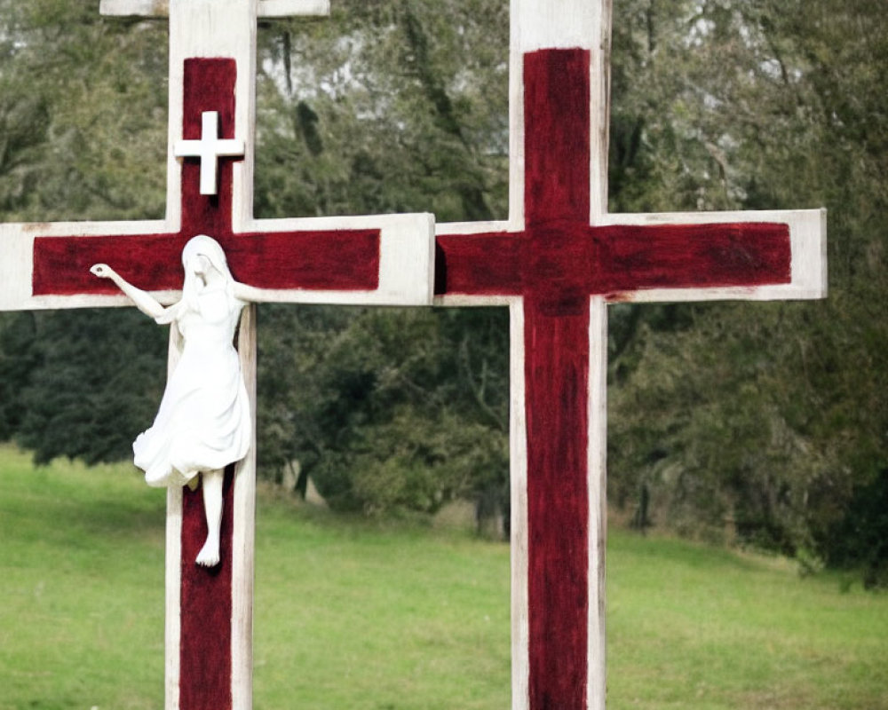 White Jesus Figure Sculpture on Cross in Grass Field with Red Details