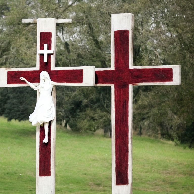 White Jesus Figure Sculpture on Cross in Grass Field with Red Details