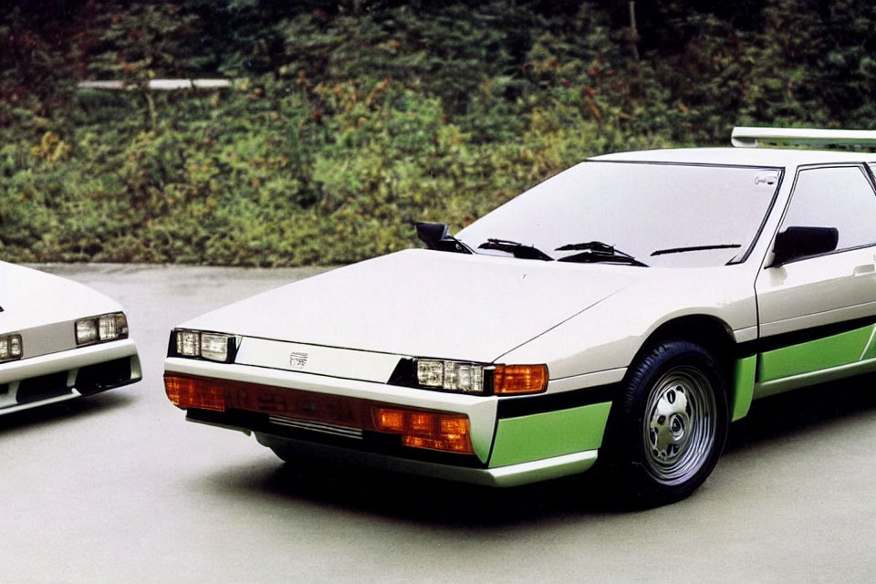 Two white sports cars with green stripes parked outdoors amidst lush greenery