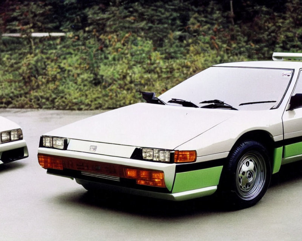 Two white sports cars with green stripes parked outdoors amidst lush greenery