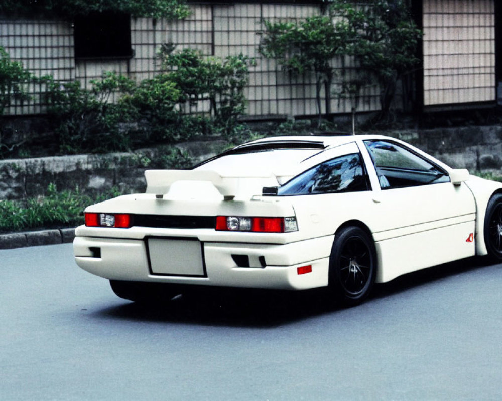 White Sports Car with Black Rims and Rear Spoiler Parked Beside Building