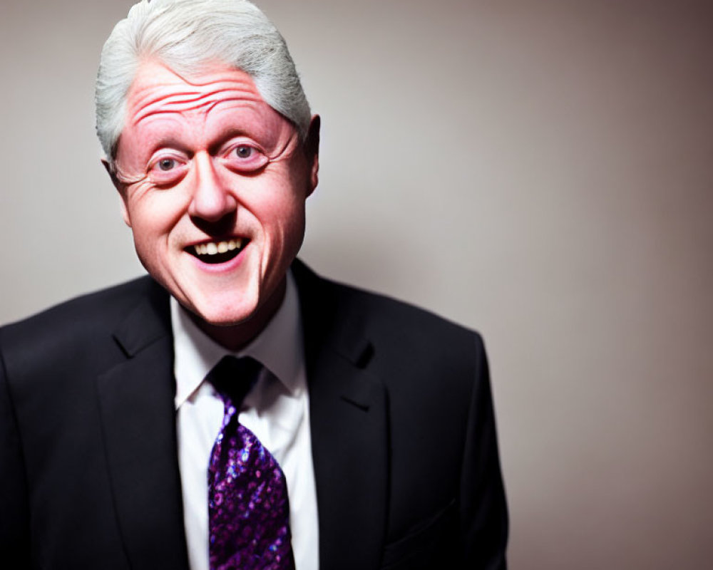 Smiling man with white hair in black suit and purple tie on pinkish-brown background