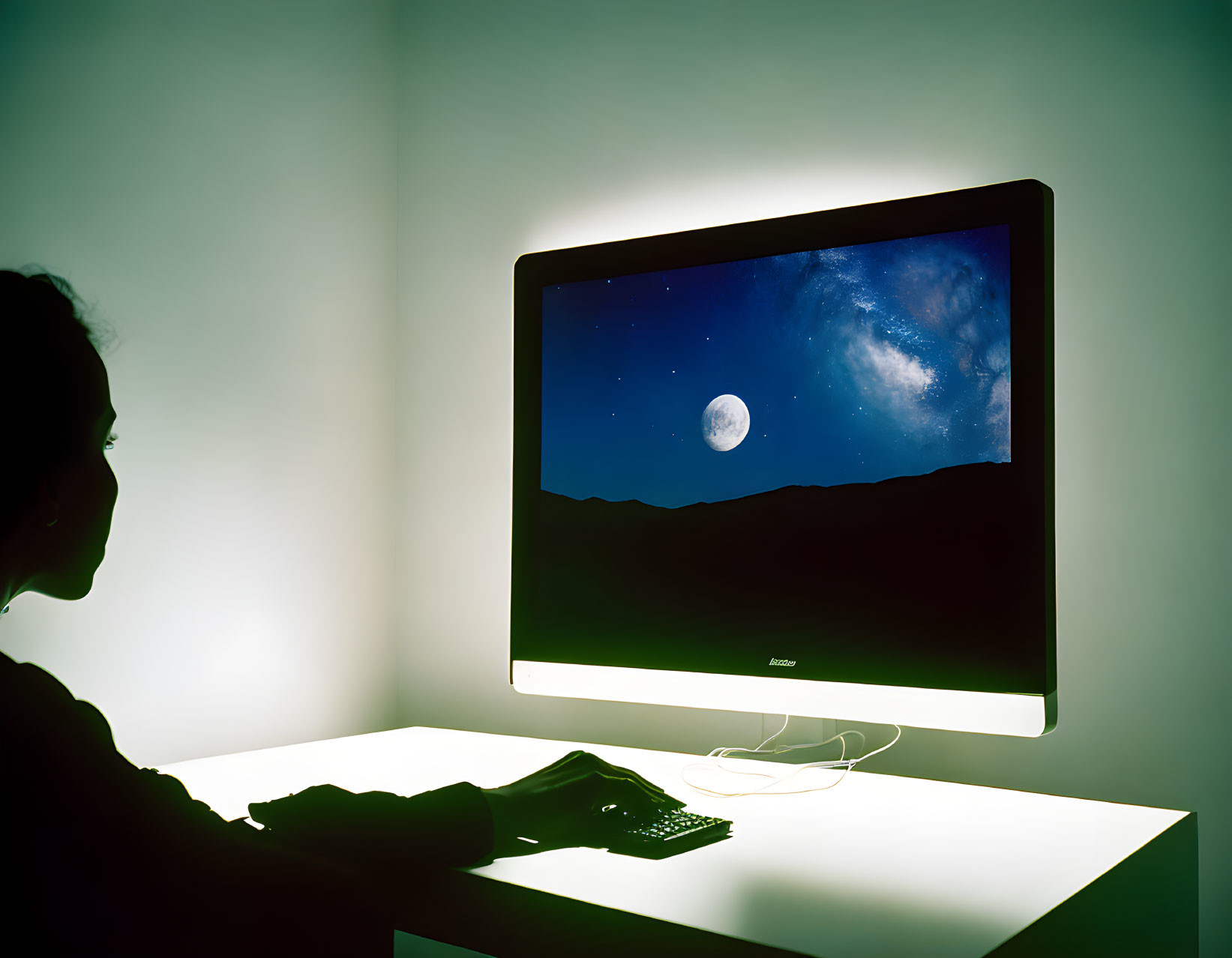 Person at desk gazes at night sky on computer screen in dimly lit room