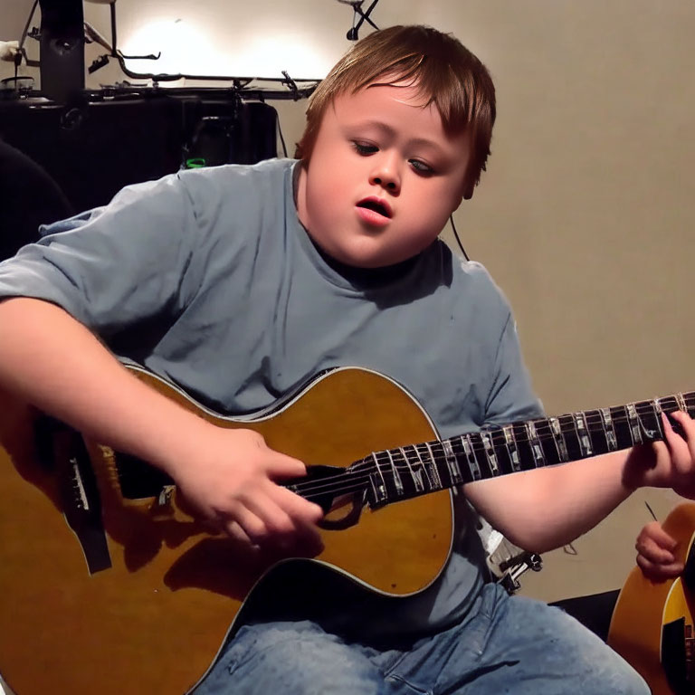 Young boy playing acoustic guitar with musical equipment in background