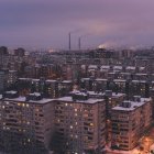 Snow-covered cityscape at dusk with residential and skyscraper buildings under twilight sky