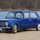 Vintage Blue Sedan with Chrome Detailing Parked by Lake Amid Green Trees