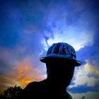 Silhouetted person with cracked head reveals ethereal figures and lightning in twilight sky