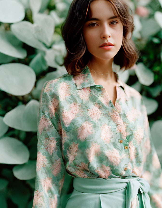 Woman in Floral Blouse Poses Among Green Foliage