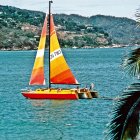 Colorful sailboat sailing in blue sea with green mountains and cloudy sky