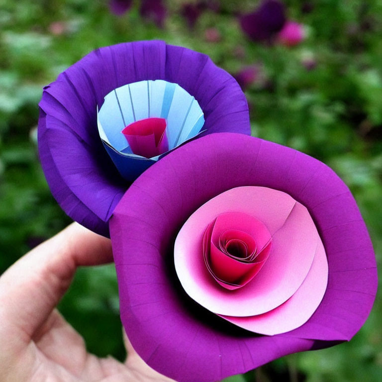 Handcrafted paper flowers: Purple and pink petals against green backdrop