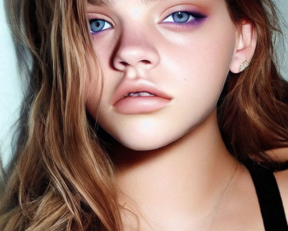 Young woman with wavy brown hair and blue eyes wearing black top and delicate necklace gazes at camera