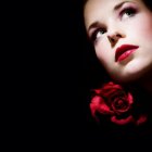 Person with Striking Blue Eyes Holding Red Rose on Dark Background