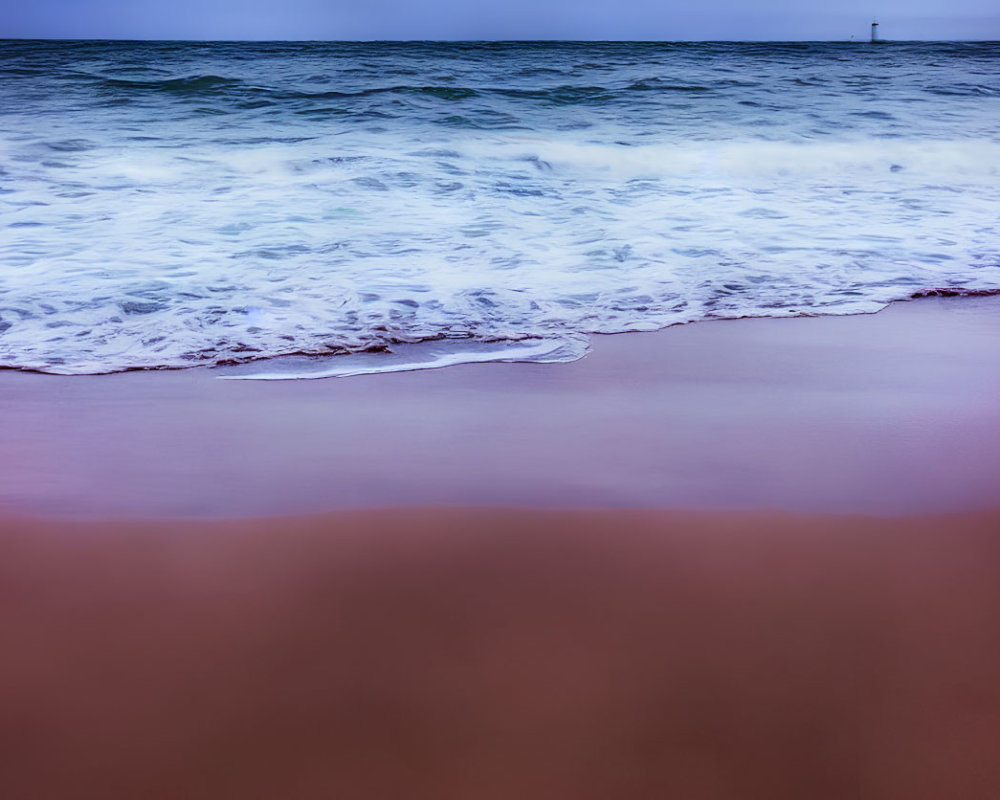 Seaside scene with ocean waves, sandy shore, and distant lighthouse