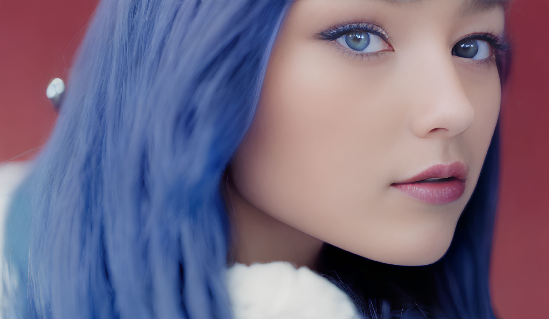 Close-up of person with striking blue hair and intense blue eyes against red background