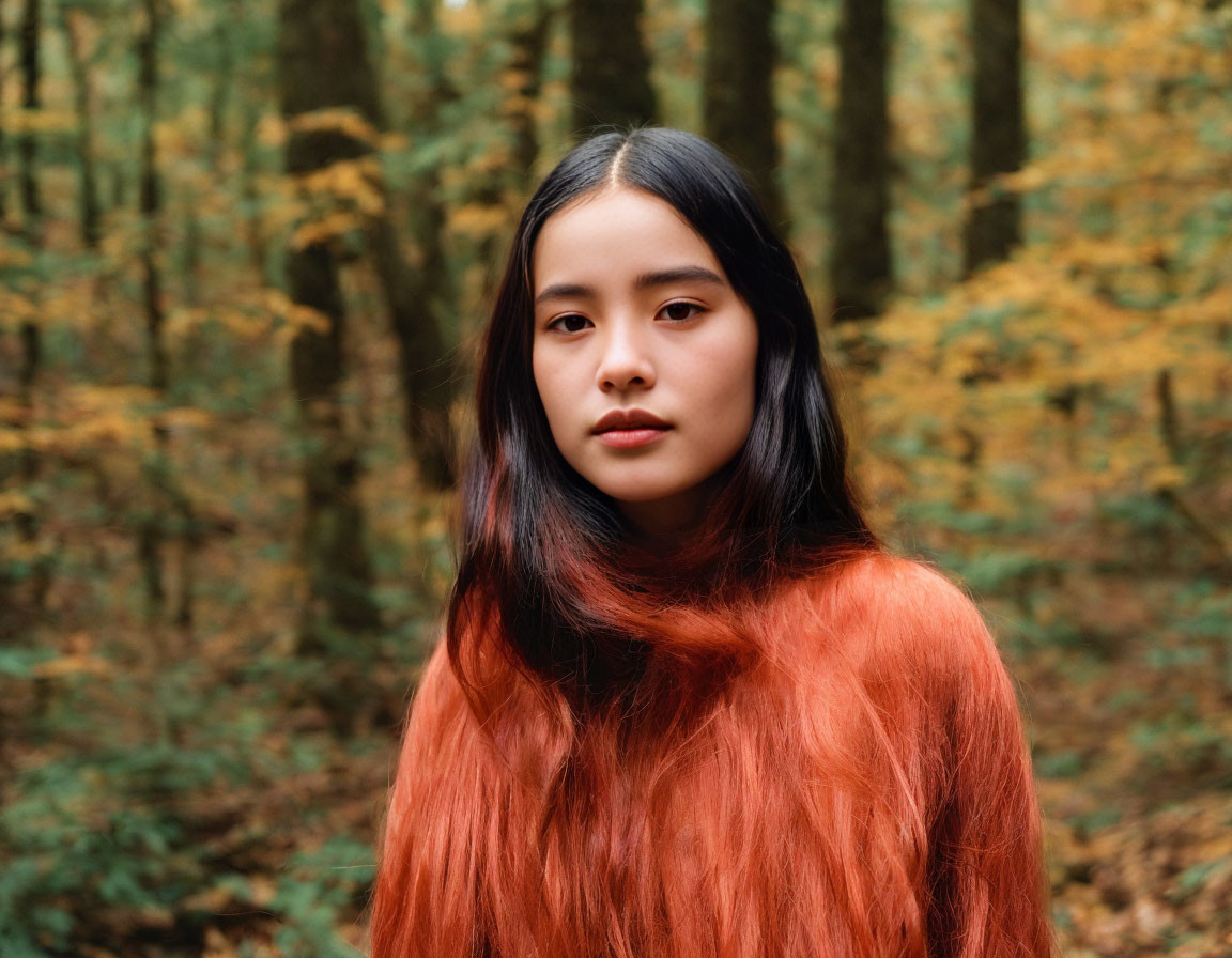 Woman with long black hair in orange sweater in autumn forest