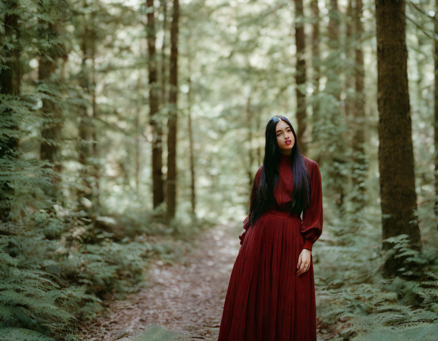 Woman in red dress on forest path with tall green trees and ferns