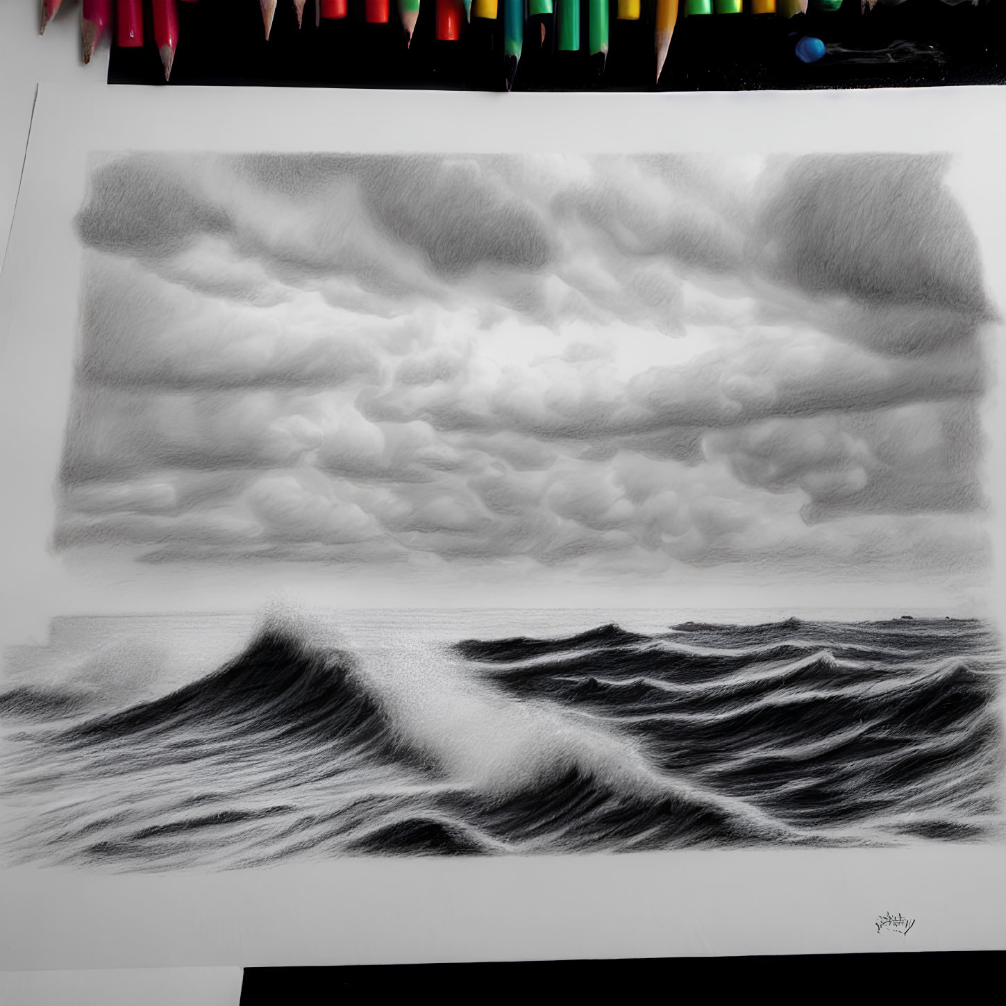 Graphite drawing of stormy sea with pencils beside it