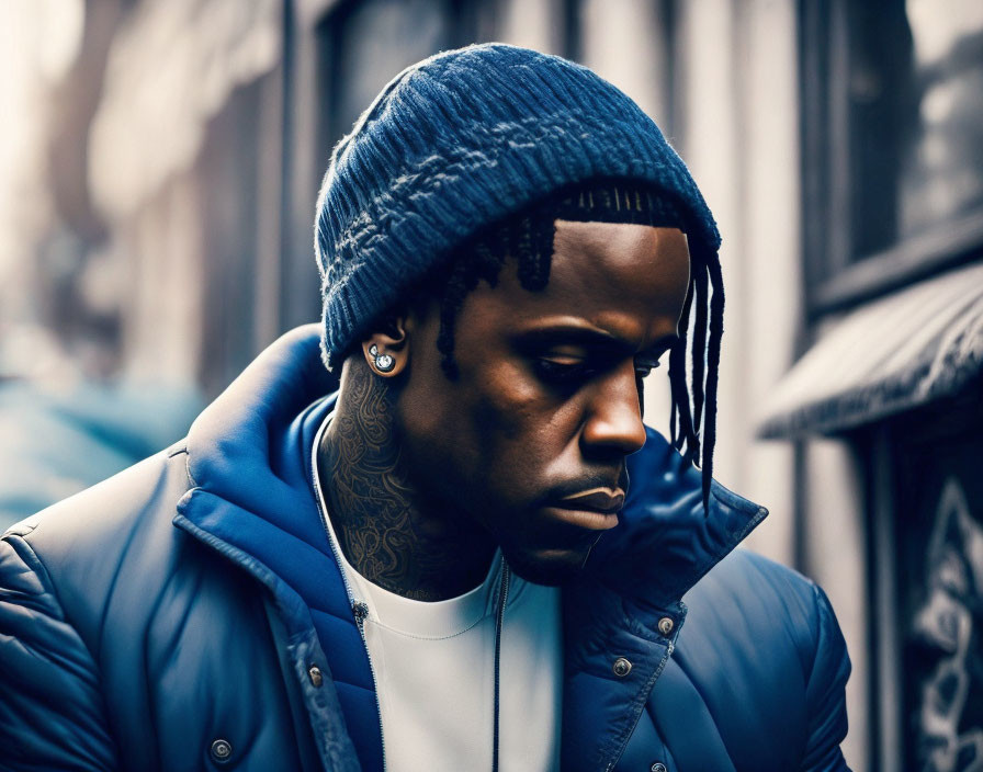 Dreadlocked man in blue beanie and tattoos against urban backdrop