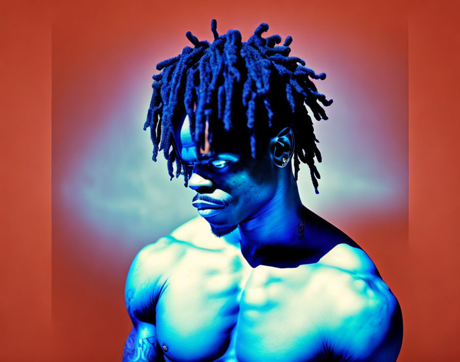 Shirtless man with dreadlocks and tattoos in blue light on orange backdrop