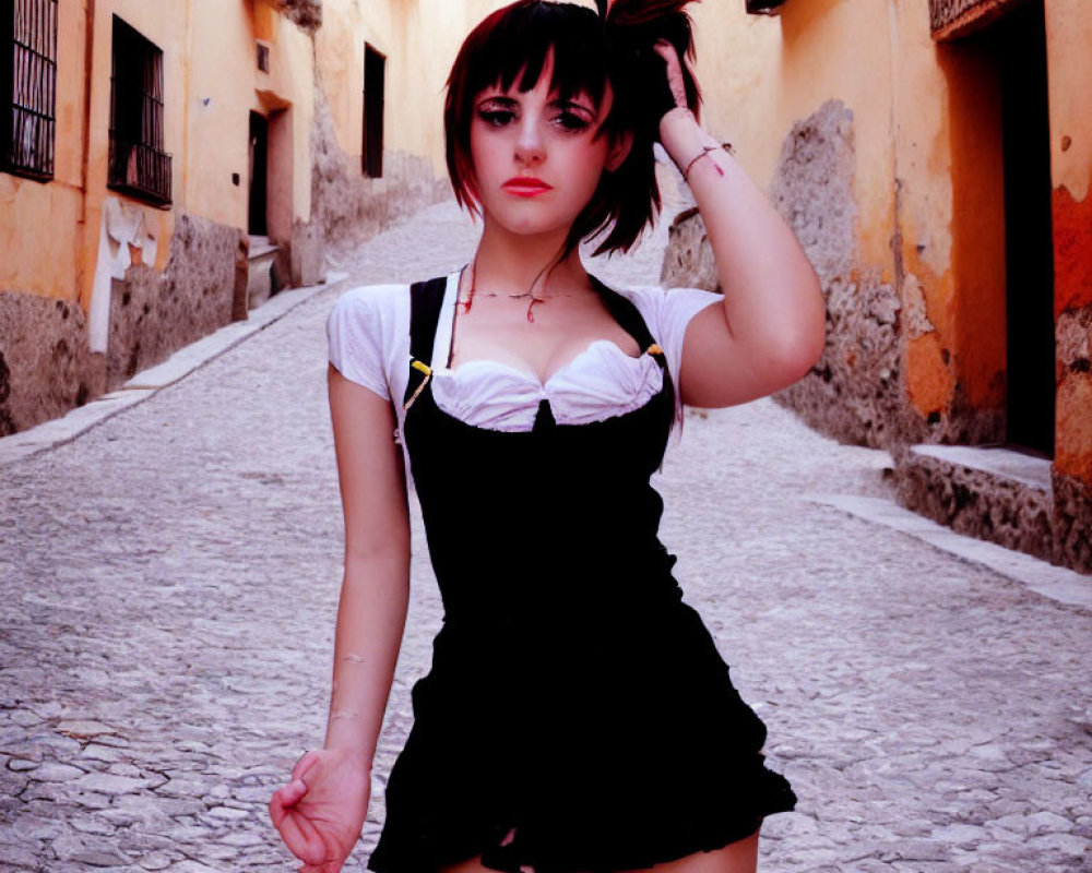 Short-haired person in white blouse and black dress on cobblestone street with pastel buildings