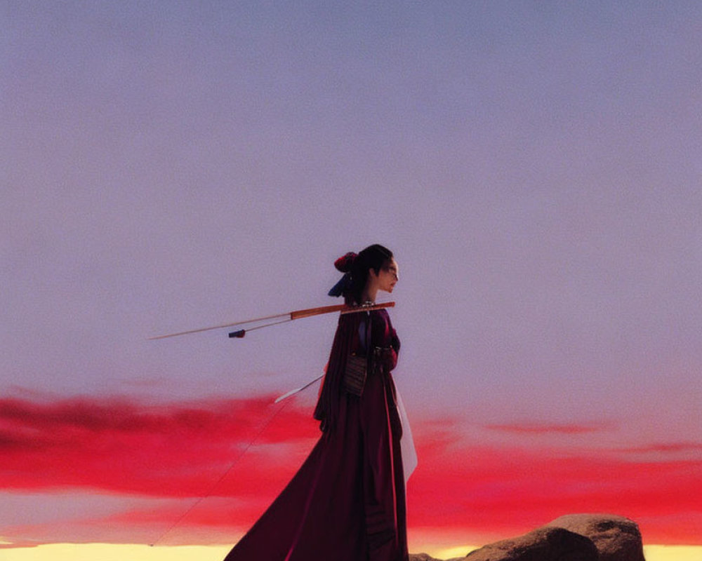 Person in Traditional Attire with Sword Gazes at Sunset Sky